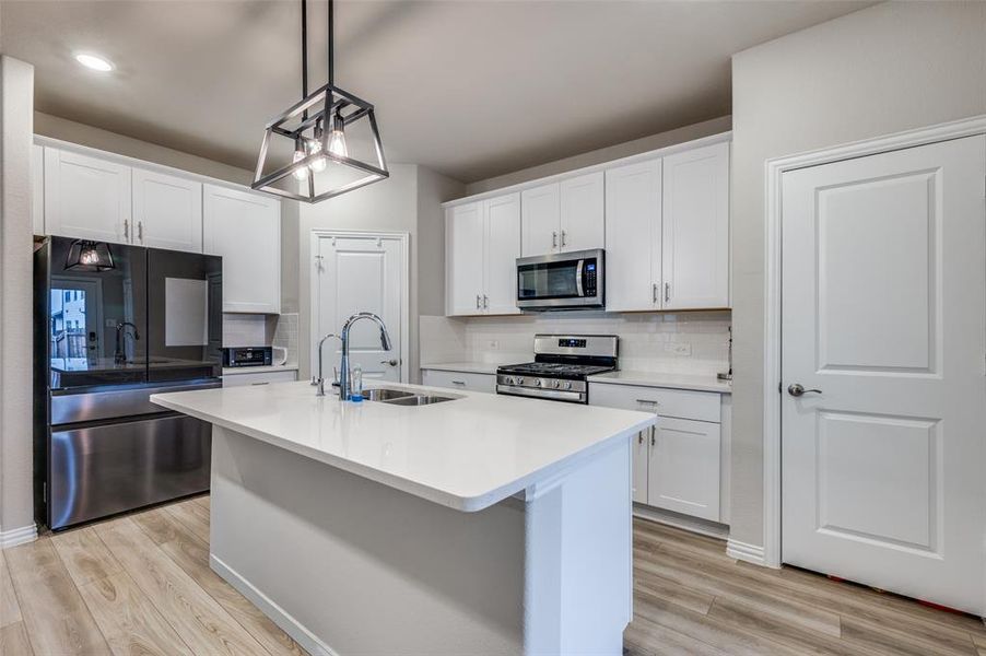 Kitchen with appliances with stainless steel finishes, a center island with sink, white cabinets, backsplash, and recessed lighting