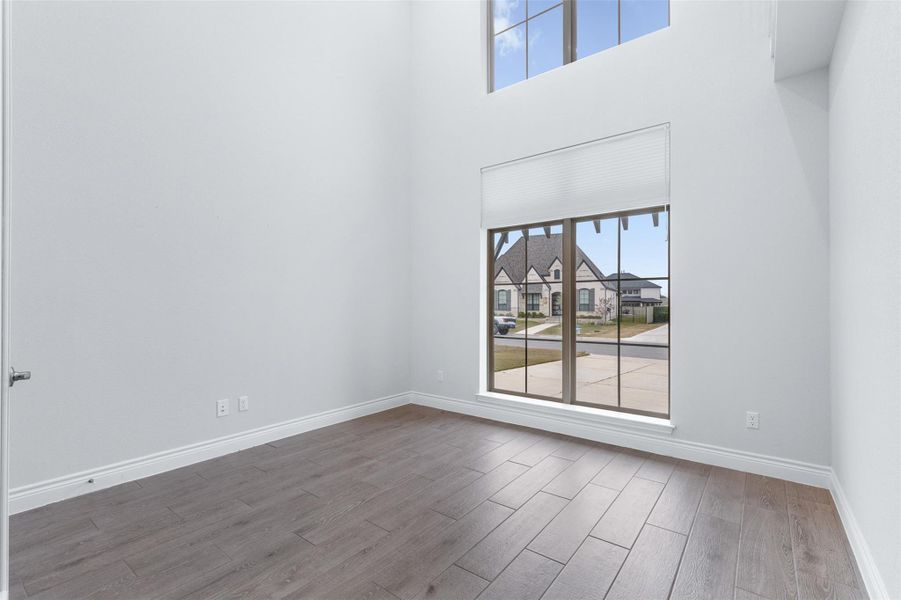 Unfurnished room featuring plenty of natural light, light wood-type flooring, a high ceiling, and a residential view