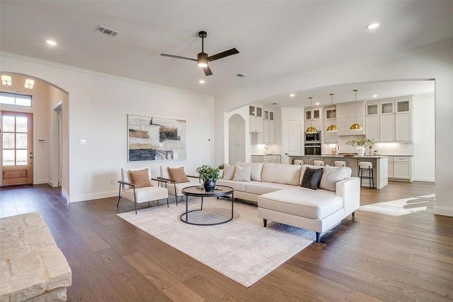 Living room featuring fireplace with stone surround, crown molding, ceiling fan, engineered wood flooring, 10 ft ceilings and 8 ft doors