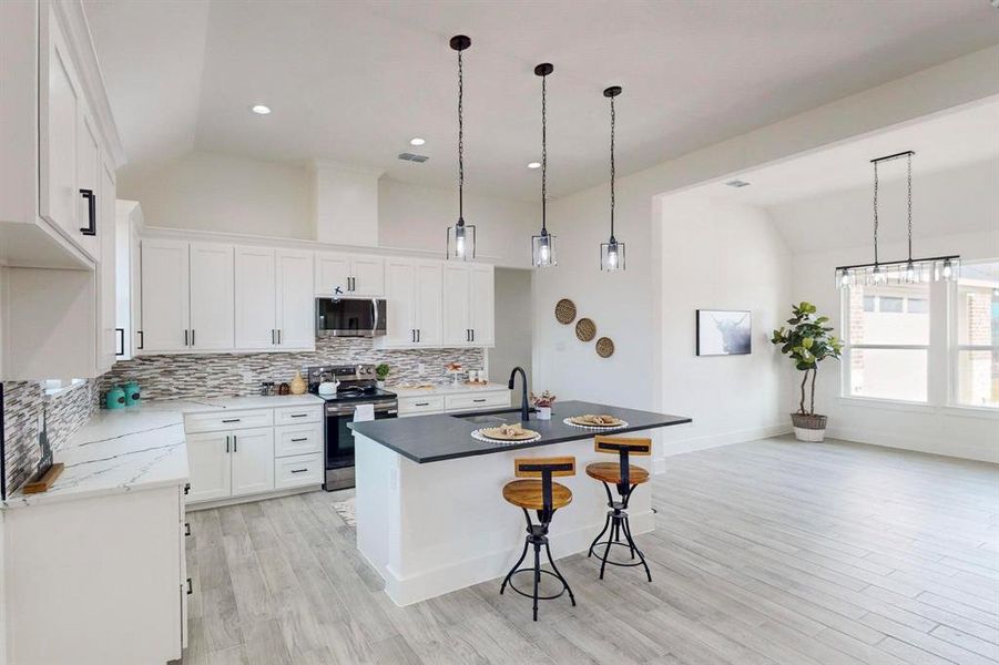 Kitchen with sink, an island with sink, vaulted ceiling, white cabinets, and appliances with stainless steel finishes