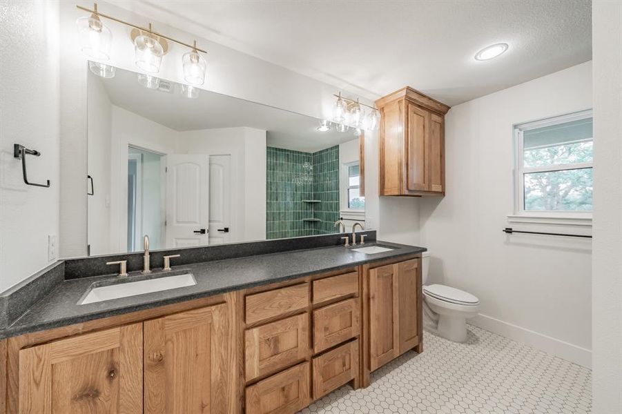 Bathroom with double vanity, toilet, plenty of natural light, and a shower