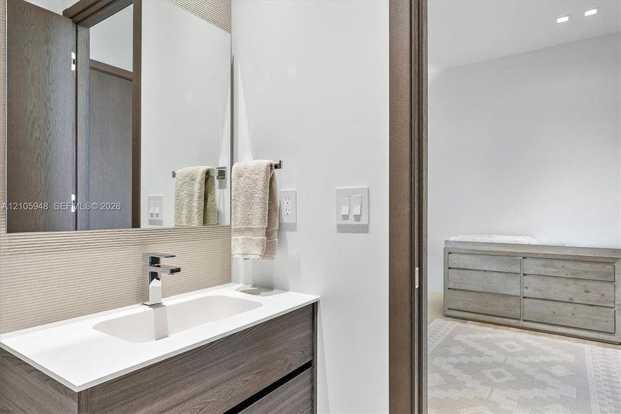 Wall-mounted mirror above a vanity featuring a wood-finish cabinet, white countertop, integrated rectangular sink, and polished chrome faucet