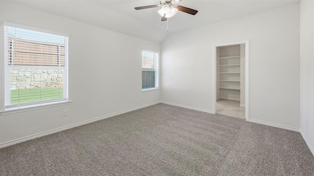 Unfurnished bedroom featuring carpet, a walk in closet, vaulted ceiling, and a ceiling fan