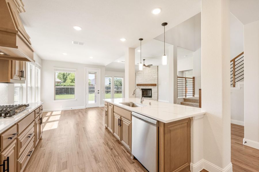 Open kitchen with wood cabinets, large island, white countertops, and hardwood floors open to living area with fireplace Open kitchen with wood cabinets, large island, white countertops, and hardwood floors open to living area with fireplace