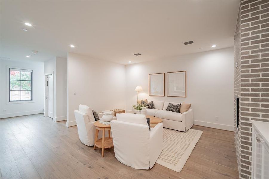 Living room with a brick fireplace and light hardwood / wood-style floors