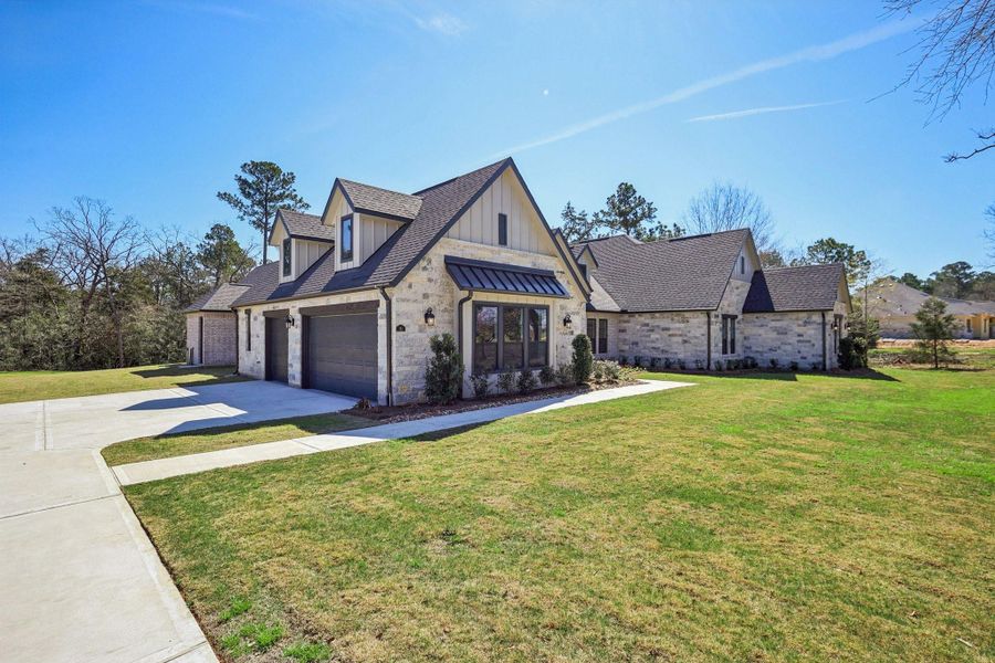 This photo showcases a charming, modern stone house with a gabled roof and a well-maintained lawn. It features a spacious driveway leading to a three-car garage.
