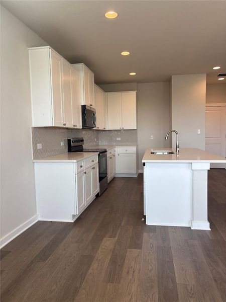 Kitchen with stainless steel appliances, white cabinetry, decorative backsplash, dark wood-style flooring, and recessed lighting