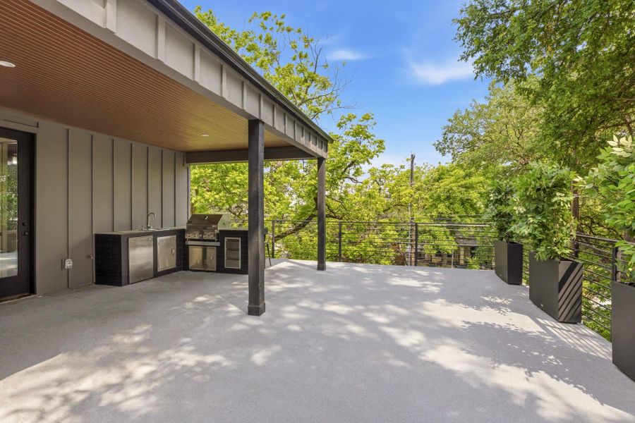 Expansive outdoor deck featuring an integrated outdoor kitchen with stainless steel appliances, a built-in sink, and a covered patio area
