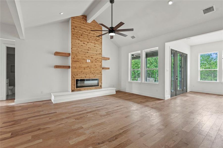 Unfurnished living room with ceiling fan, beam ceiling, wood finished floors, a large fireplace, and high vaulted ceiling