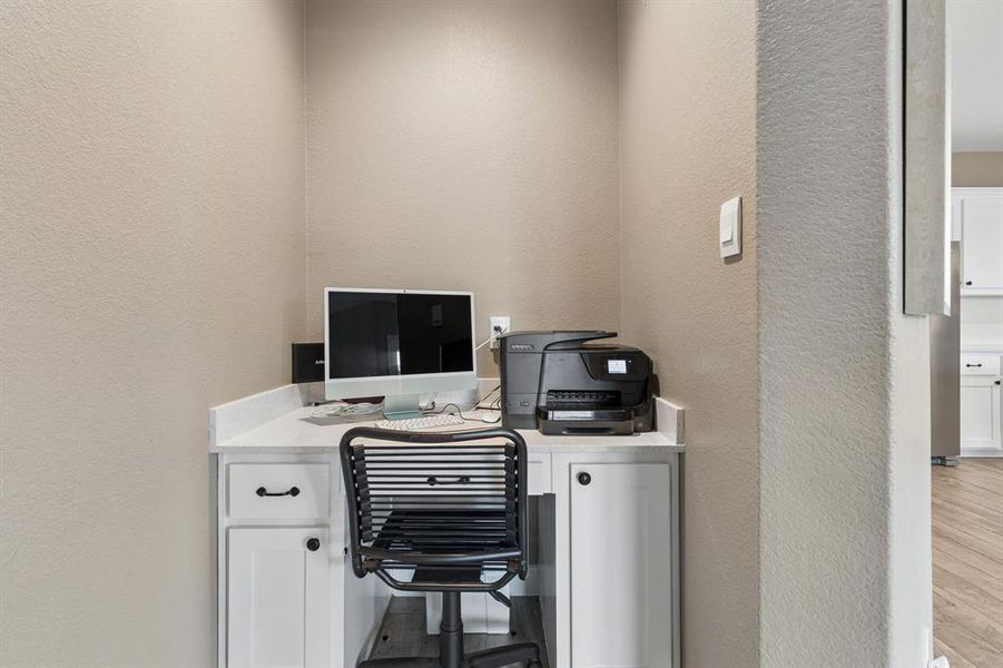 Built-in desk featuring a white countertop, base cabinetry with black hardware, and an open knee space
