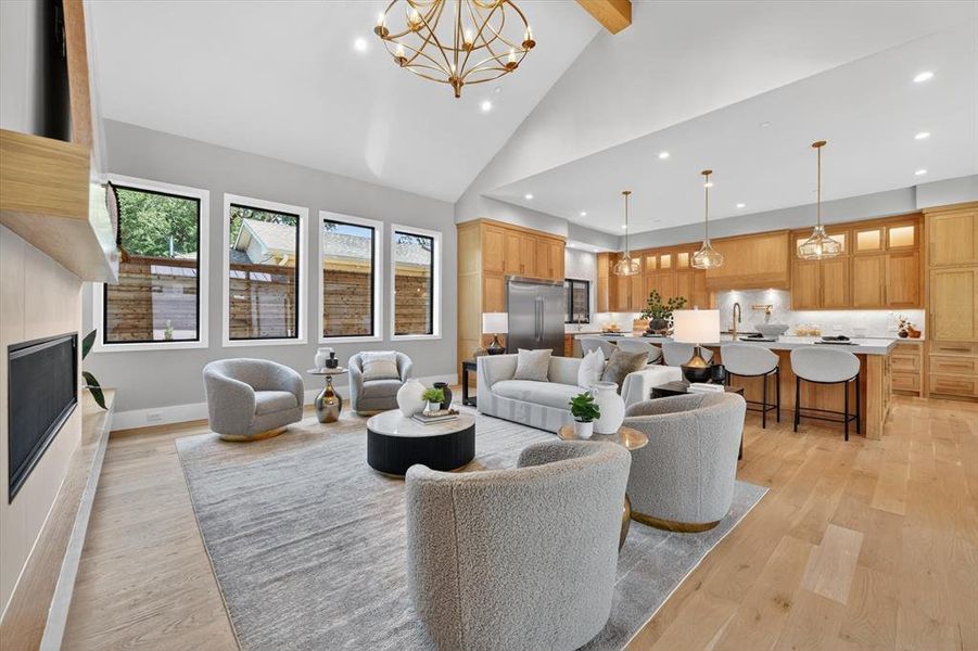 Spacious open-concept living area featuring high vaulted ceilings with exposed beam, a built-in fireplace with a light wood-finish surround, light wood-finish flooring, and a kitchen with warm wood cabinetry, a large island, and pendant lighting Spacious open-concept living area featuring high vaulted ceilings with exposed beam, a built-in fireplace with a light wood-finish surround, light wood-finish flooring, and a kitchen with warm wood cabinetry, a large island, and pendant lighting