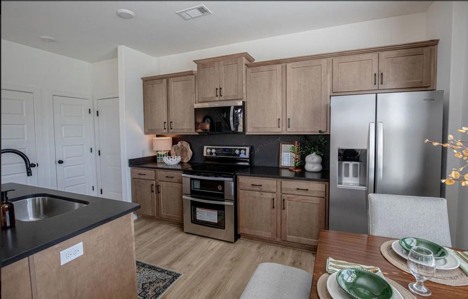 Kitchen with stainless steel appliances, light wood finished floors, and dark stone countertops