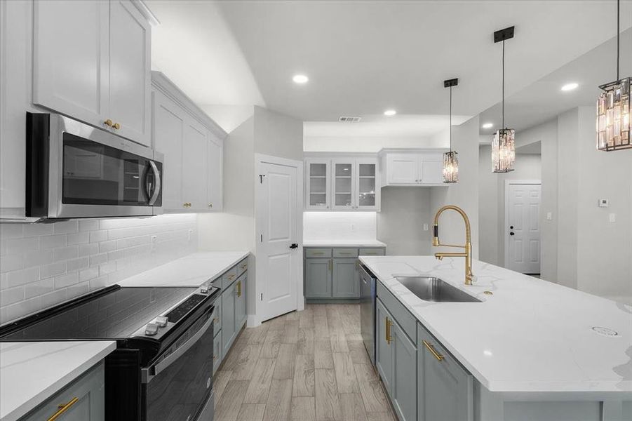 Kitchen featuring stainless steel appliances, a sink, white cabinetry, light wood-type flooring, and backsplash