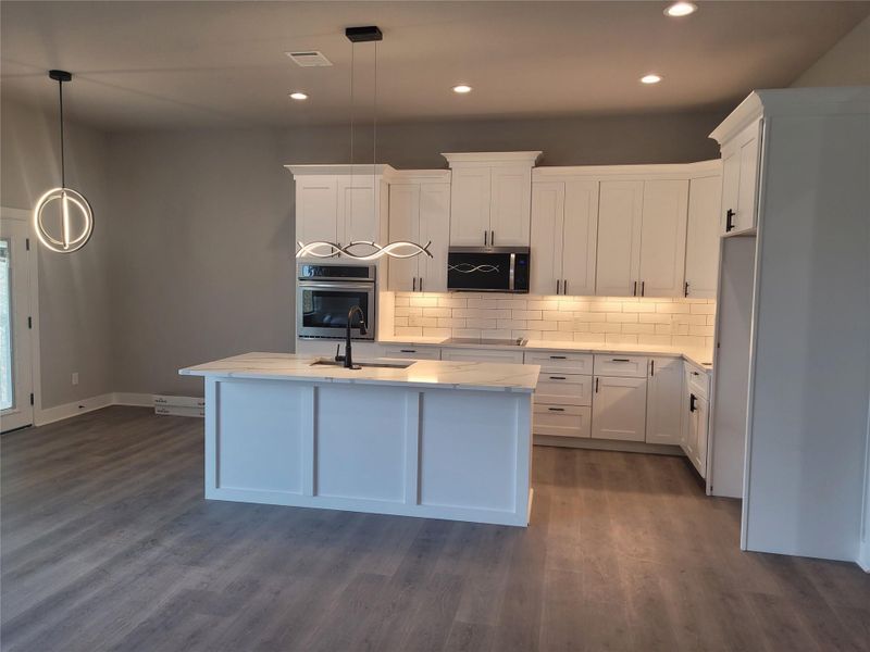Kitchen with a center island with sink, white cabinets, stainless steel appliances, light stone countertops, and dark wood-style flooring