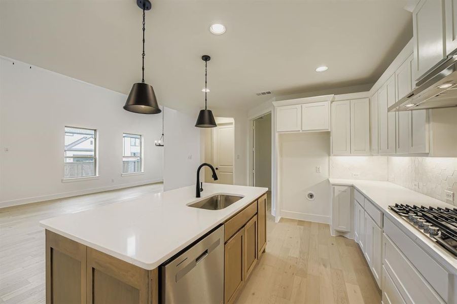 Kitchen with light wood-style flooring, white cabinets, appliances with stainless steel finishes, decorative light fixtures, and decorative backsplash Kitchen with light wood-style flooring, white cabinets, appliances with stainless steel finishes, decorative light fixtures, and decorative backsplash