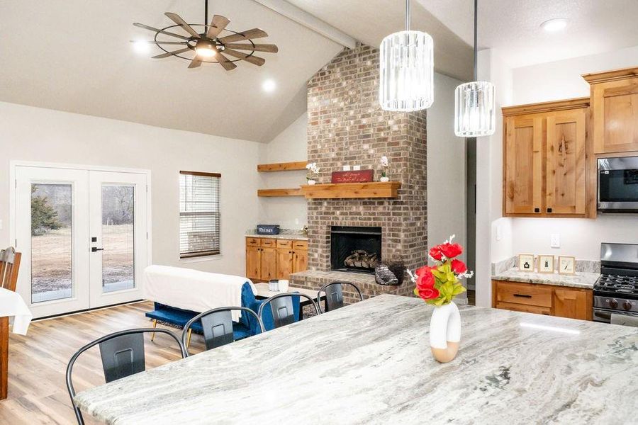 Dining space featuring a fireplace, lofted ceiling with beams, ceiling fan, light wood-type flooring, and french doors