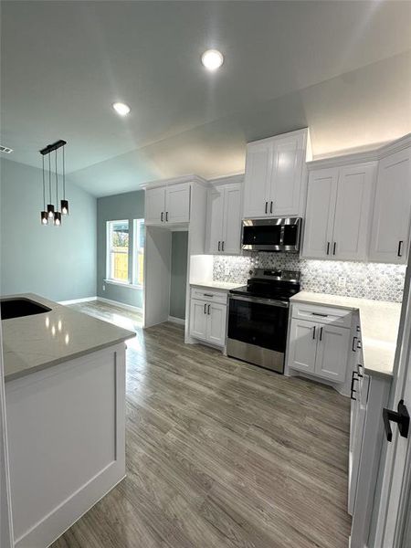 Kitchen with decorative backsplash, stainless steel appliances, pendant lighting, white cabinetry, and light hardwood / wood-style floors