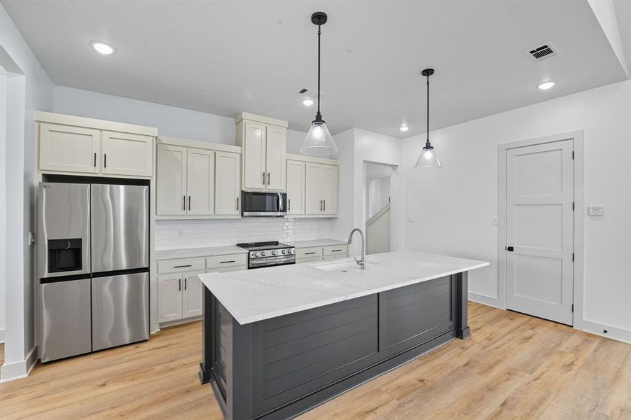 Kitchen with appliances with stainless steel finishes, decorative backsplash, pendant lighting, light wood finished floors, and recessed lighting Kitchen with appliances with stainless steel finishes, decorative backsplash, pendant lighting, light wood finished floors, and recessed lighting