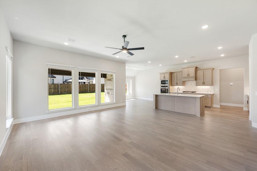 Open living area with light wood floors, ceiling fan, and kitchen island with tan cabinets in background