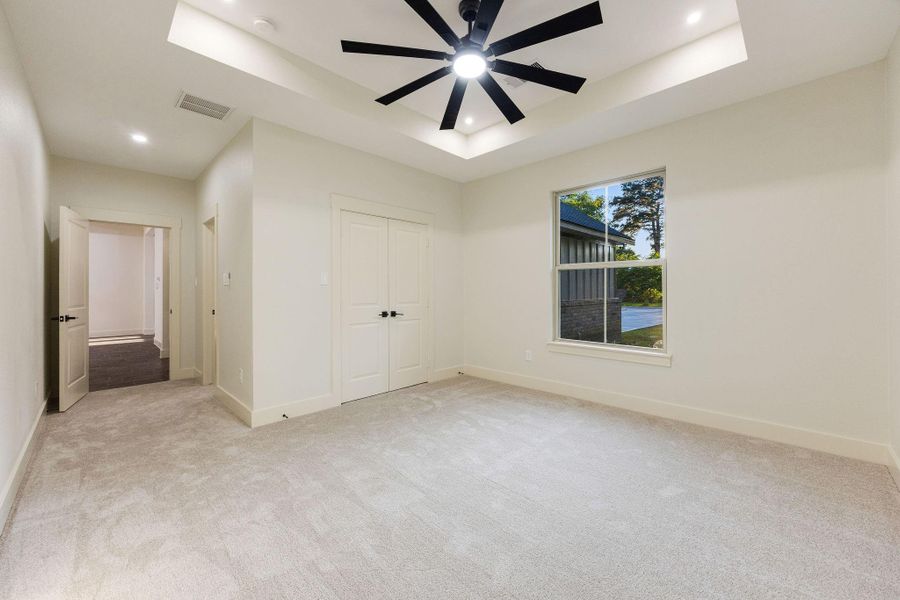 This secondary carpeted bedroom features a modern ceiling fan and recessed lighting. It has a large window for natural light, a double-door closet, and a clean, neutral color scheme.