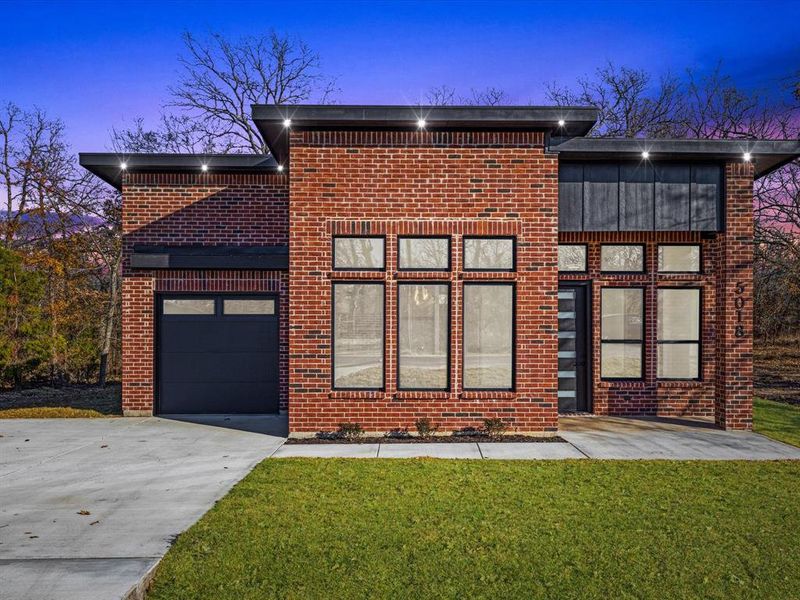 Contemporary house with driveway, brick siding, a garage, and a yard