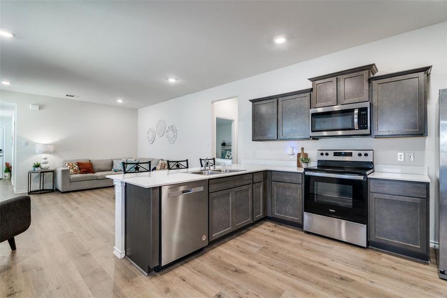 Kitchen with a peninsula, a sink, open floor plan, light countertops, and appliances with stainless steel finishes