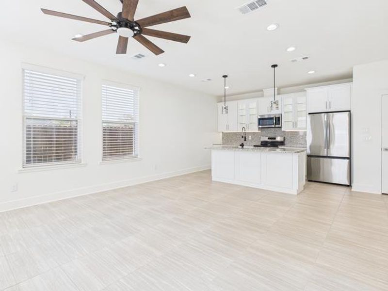 Kitchen with open floor plan, appliances with stainless steel finishes, decorative light fixtures, a center island with sink, and white cabinetry Kitchen with open floor plan, appliances with stainless steel finishes, decorative light fixtures, a center island with sink, and white cabinetry