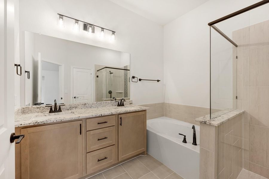 Bathroom with double vanity, granite countertops, soaking tub, and glass shower with tile surround