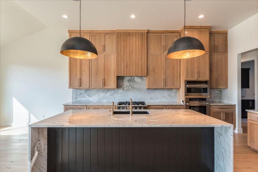 The stunning center island is complemented by custom cabinetry with a natural stain finish and is equipped with Thor stainless appliances. The cabinet pulls are finished in champagne bronze, paired with sleek pendant lighting.