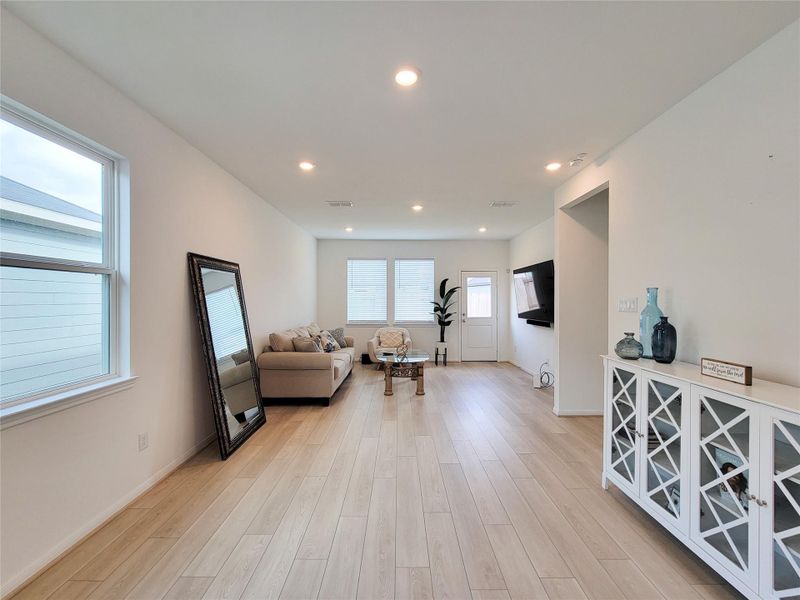 This bright, modern living room features light wood flooring, neutral walls, and ample natural light from large windows.