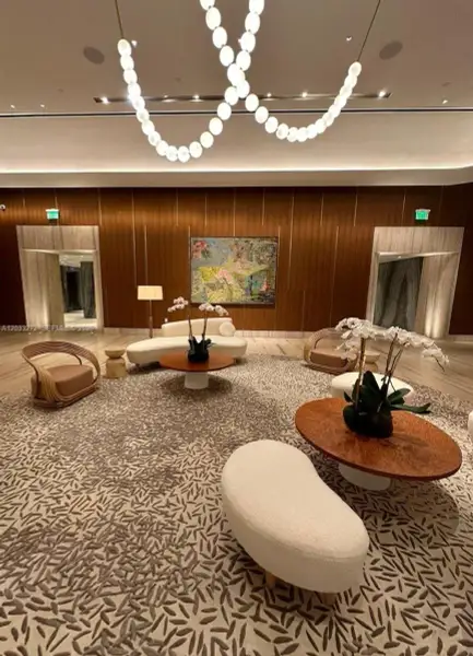 Lobby featuring vertical wood-paneled walls, stone-surround recessed entryways, patterned wall-to-wall carpeting, and a custom circular-link ceiling fixture Lobby featuring vertical wood-paneled walls, stone-surround recessed entryways, patterned wall-to-wall carpeting, and a custom circular-link ceiling fixture