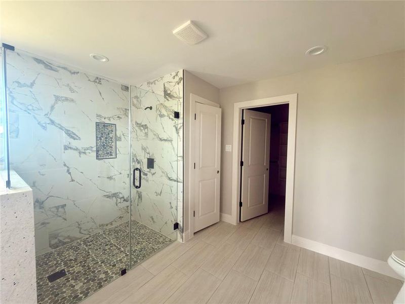 Spacious shower with clear glass enclosure, marble-look tile walls, and pebble-finish floor