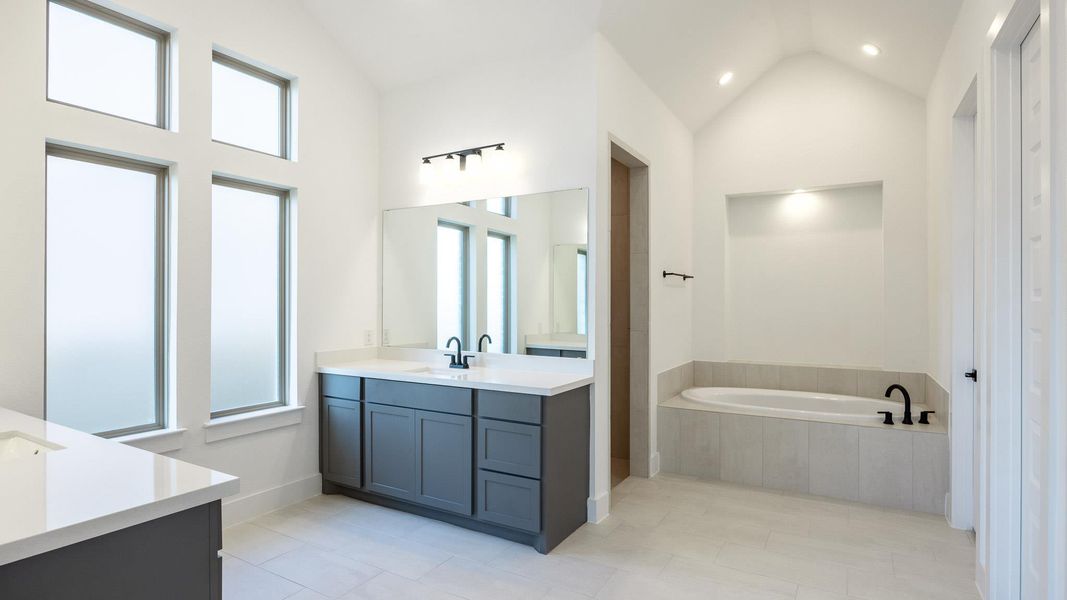 Bathroom with two vanities, a bath, tile patterned flooring, and high vaulted ceiling Bathroom with two vanities, a bath, tile patterned flooring, and high vaulted ceiling