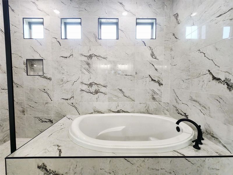 Freestanding soaking tub with a matte black faucet set against large-format marble-look wall tiles