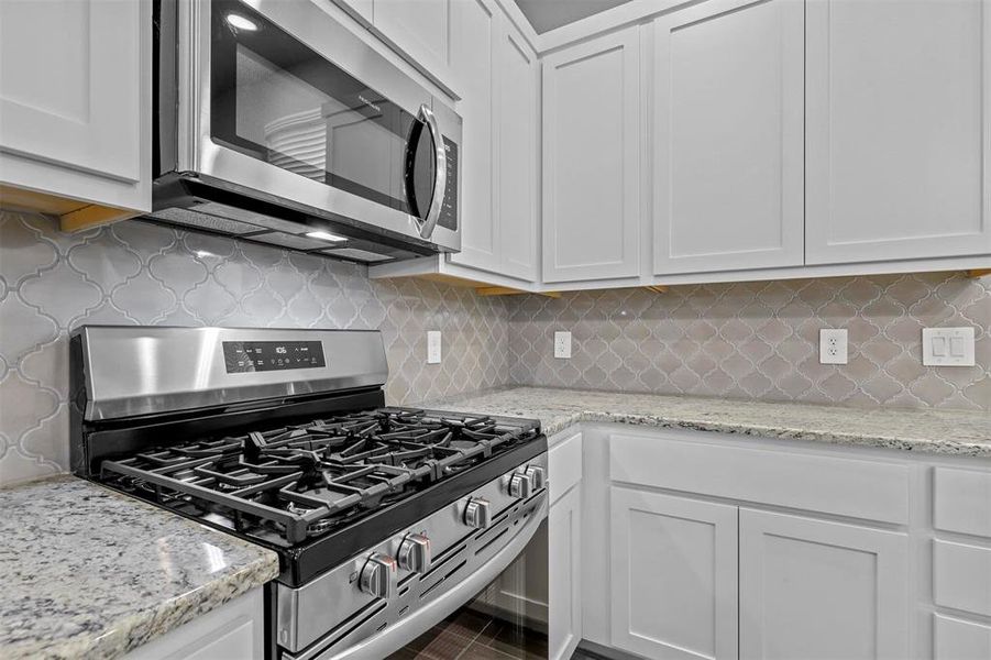 Kitchen featuring white cabinets, appliances with stainless steel finishes, backsplash, and light stone countertops