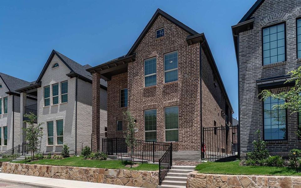 Brick exterior featuring a gabled roofline, multiple windows, a stone retaining wall, black metal fencing, and a concrete staircase