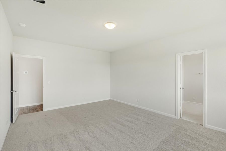 Empty bedroom with gray carpet, white walls, and two open doors leading to adjoining rooms