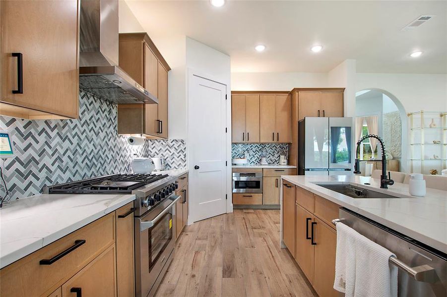 Kitchen featuring stainless steel appliances, light stone countertops, wall chimney range hood, tasteful backsplash, and recessed lighting Kitchen featuring stainless steel appliances, light stone countertops, wall chimney range hood, tasteful backsplash, and recessed lighting