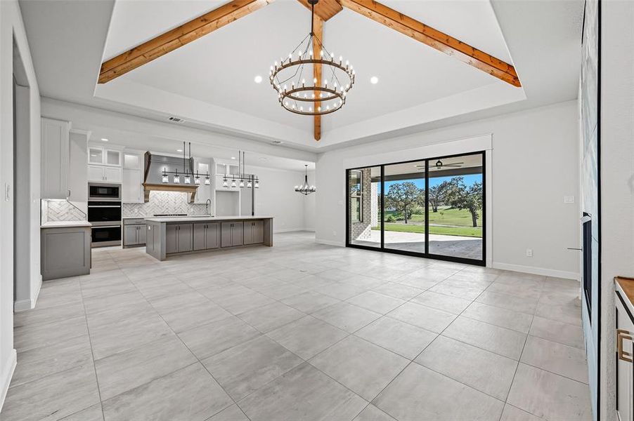 Unfurnished living room with a chandelier, a raised ceiling, beamed ceiling, recessed lighting, and light tile patterned flooring Unfurnished living room with a chandelier, a raised ceiling, beamed ceiling, recessed lighting, and light tile patterned flooring