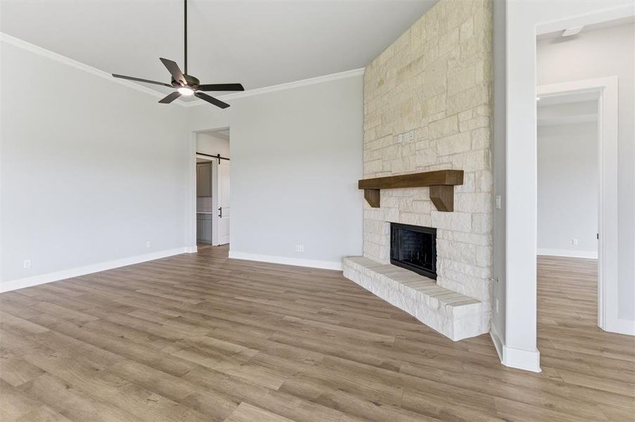 Unfurnished living room with a barn door, ceiling fan, light wood finished floors, a fireplace, and crown molding