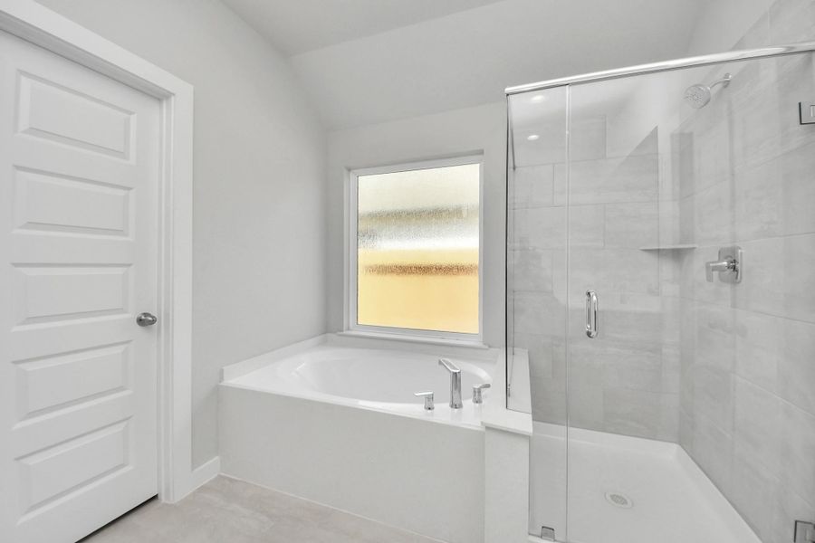 Escape to a spa-like oasis in this primary bathroom. Enjoy a walk-in shower with tile surround, a separate garden tub with custom detailing, and an elegant vanity featuring light countertops, modern hardware, and beautiful recessed lights. Experience luxury and relaxation in every detail. Sample photo of completed home with similar floor plan. Actual colors and selections may vary.