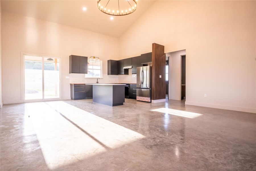 Kitchen with a chandelier, a kitchen island, open floor plan, freestanding refrigerator, and high vaulted ceiling