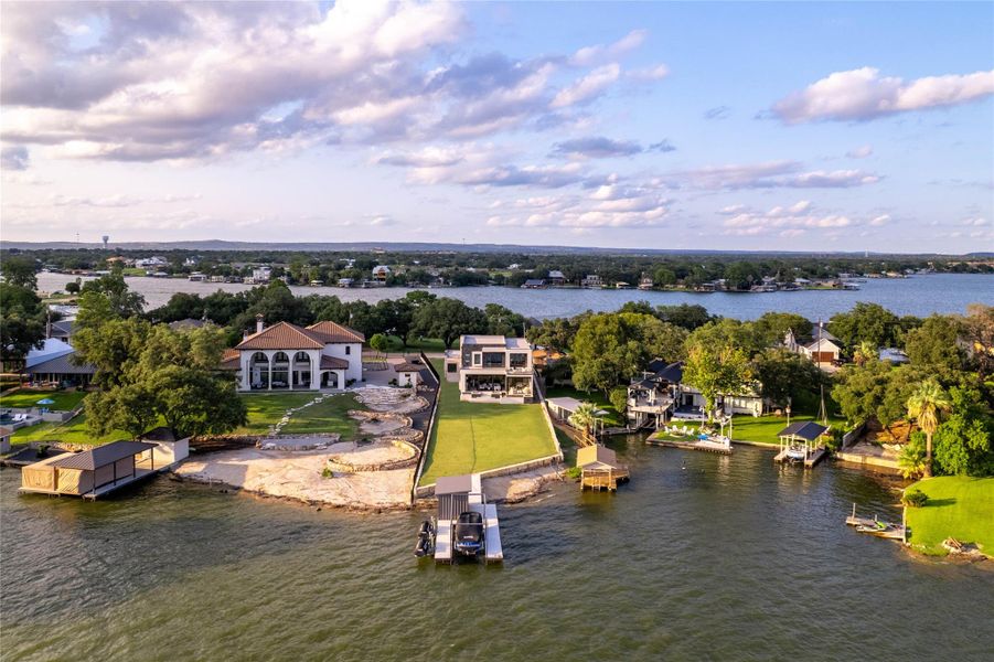 Waterfront property featuring a contemporary residence, an expansive manicured lawn, a private boat dock with a lift, and a sandy beach area