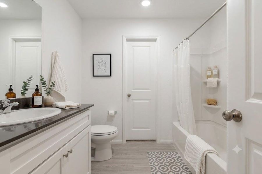 A well-lit bathroom features a vanity with a dark countertop and a combined shower-bathtub unit.