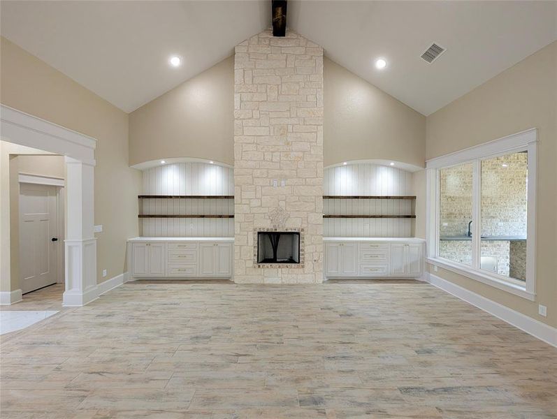 Unfurnished living room with a stone fireplace, high vaulted ceiling, light wood finished floors, beamed ceiling, and recessed lighting