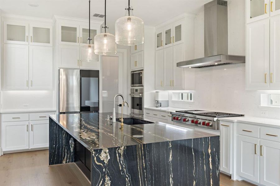 Kitchen with wall chimney exhaust hood, light wood-style flooring, stainless steel appliances, an island with sink, and white cabinets