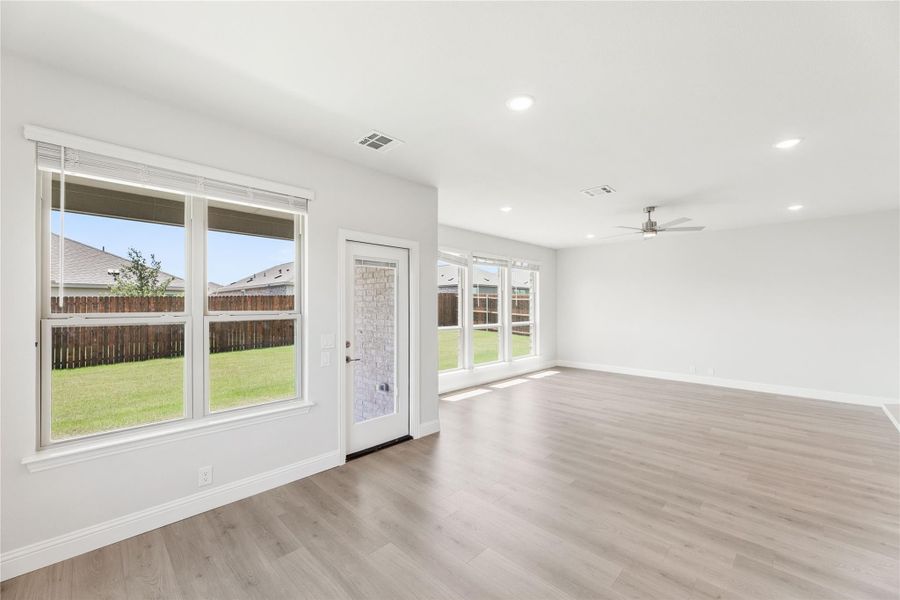 Open living room with light wood floors, ceiling fan, and large windows overlooking backyard
