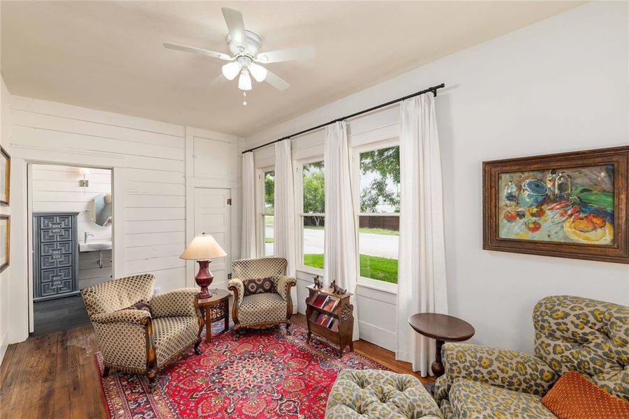 Living space featuring wood-finish flooring, white shiplap walls, a ceiling fan with integrated lighting, and multiple windows