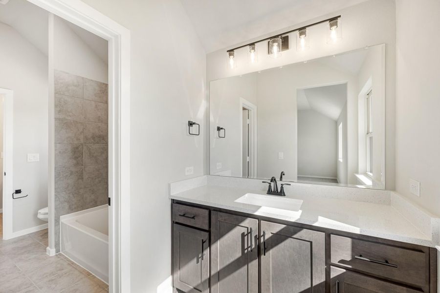 Bathroom with dark wood vanity, white quartz countertop, large mirror, and separate soaking tub with tile surround visible through doorway.