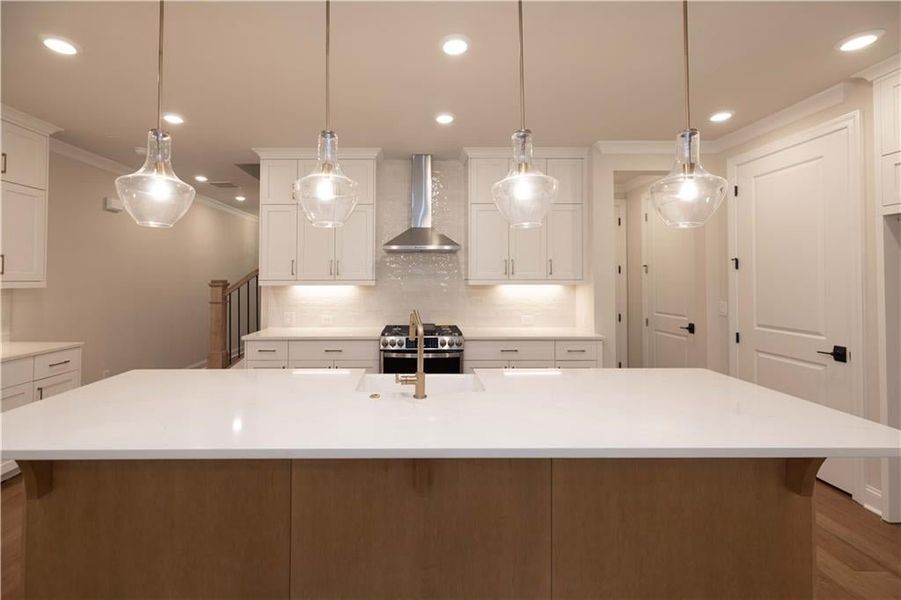Kitchen with pendant lighting, white cabinets, wall chimney exhaust hood, tasteful backsplash, and crown molding